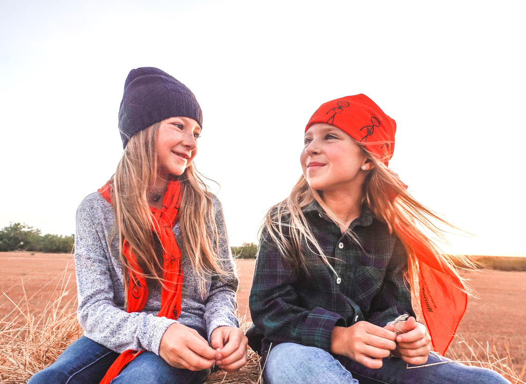 2 people wearing the triangular bandage multi tool. one wearing it as a scarf and on wearing it wrapped on their head